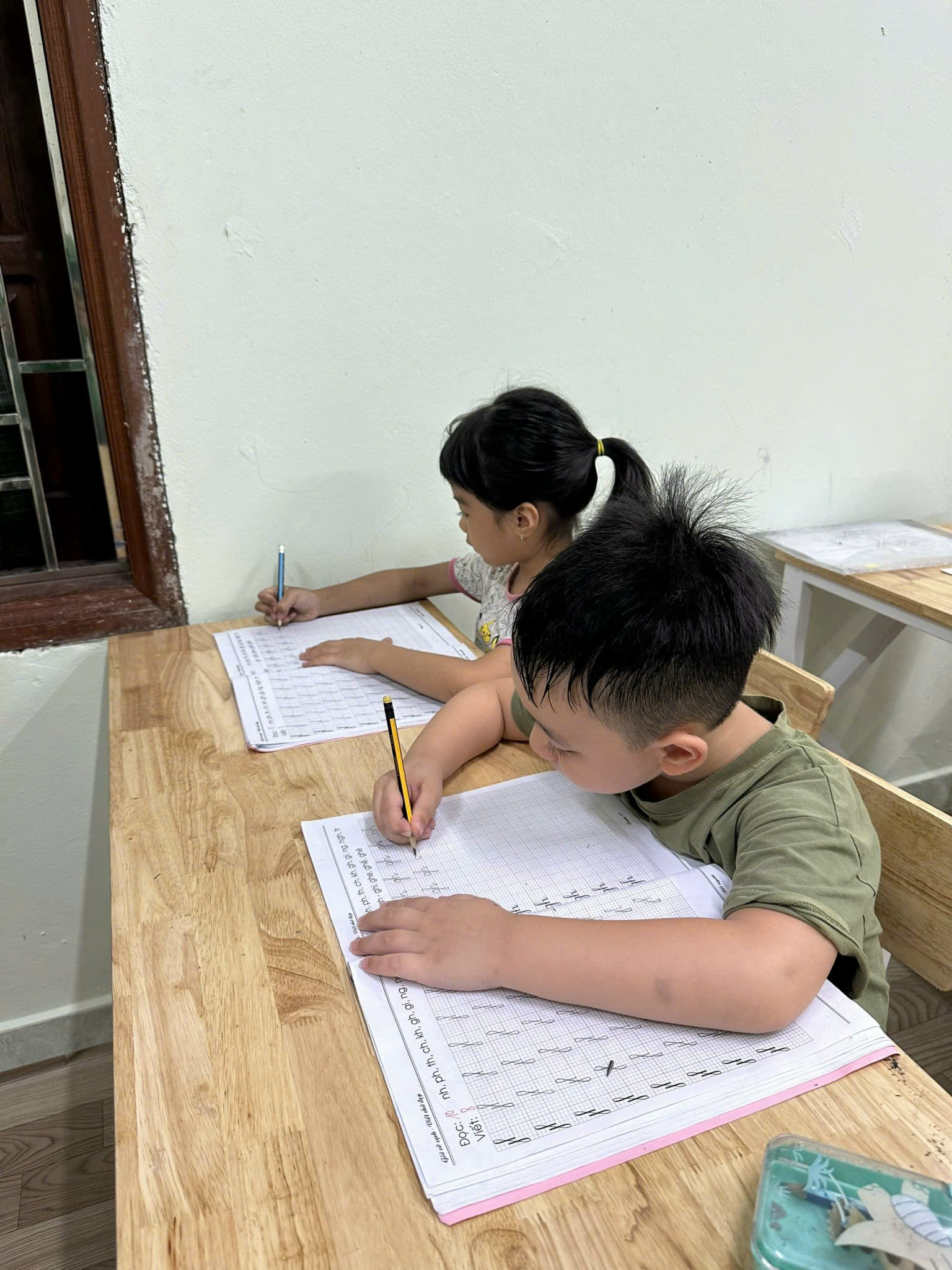 Cô giáo ngồi cạnh hướng dẫn học sinh làm bài trong lớp kèm học buổi tối của Happy Homeschool